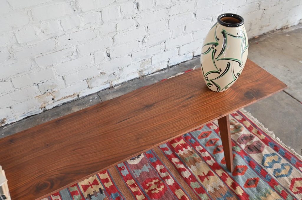 a mid century ceramic vase on top of a walnut sculpted furniture