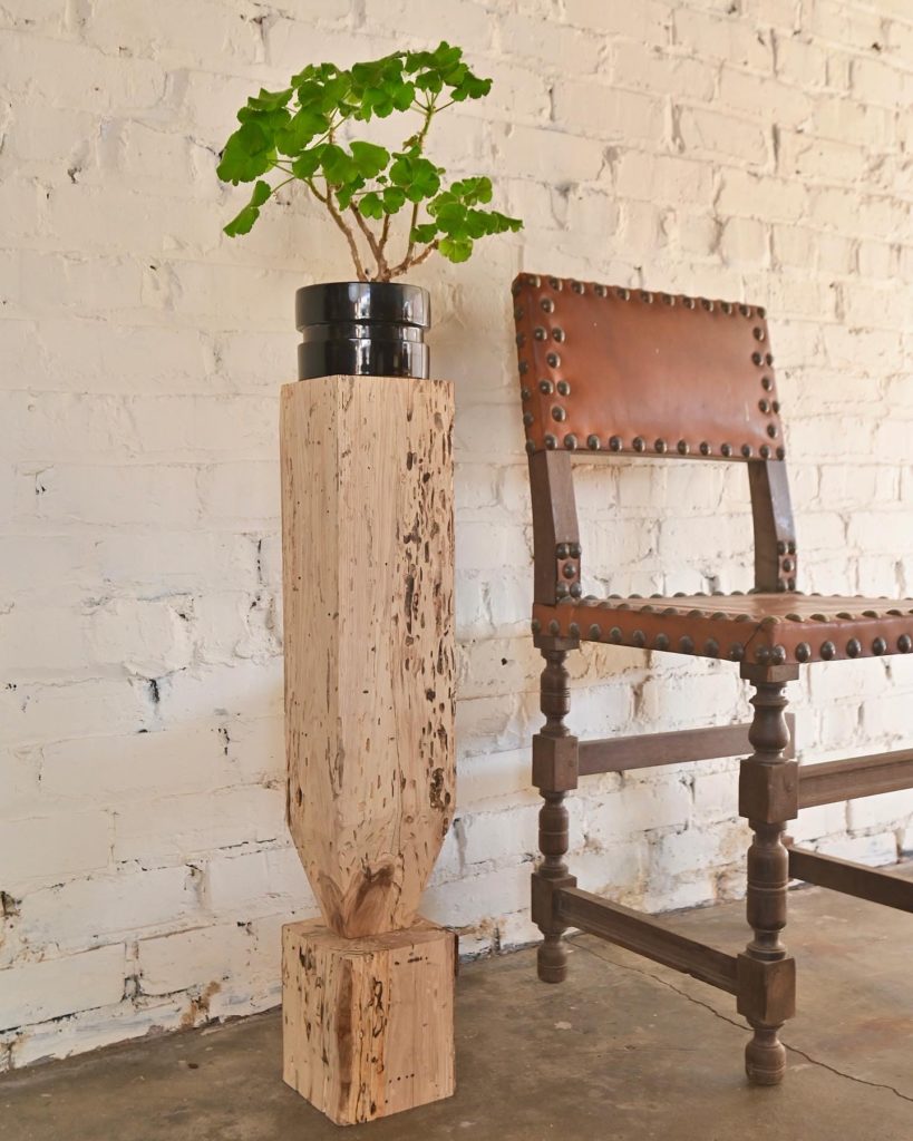antique leather chair with plant on pedestal in front of brick wall